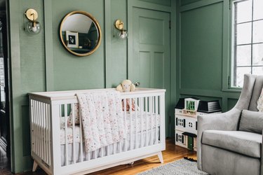 Green baby nursery idea with white crib and mirror hanging on wall with wall sconces