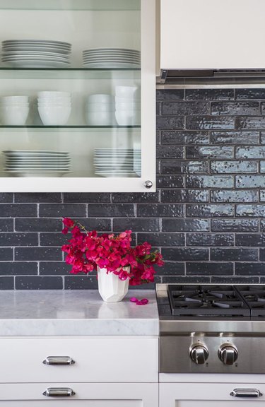 white glass kitchen cabinet with black backsplash and vase with red flowers