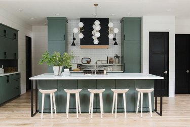 green kitchen with white stools and mid-century modern chandelier