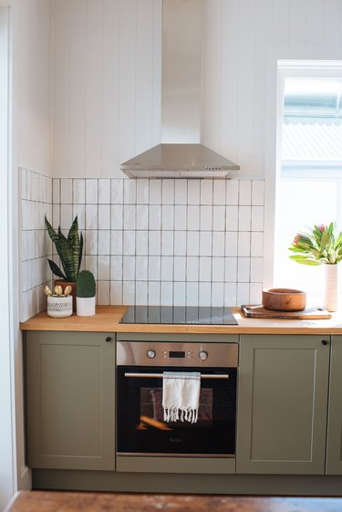 white subway tile kitchen backsplash installed vertically with green cabinets and wood countertop