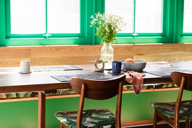 green window trim behind a wood breakfast table with wood chairs and flower on the table