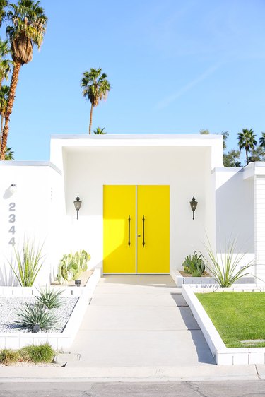 Yellow midcentury modern front door with white exterior and palm trees