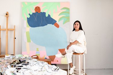 woman sitting on stool near large painting