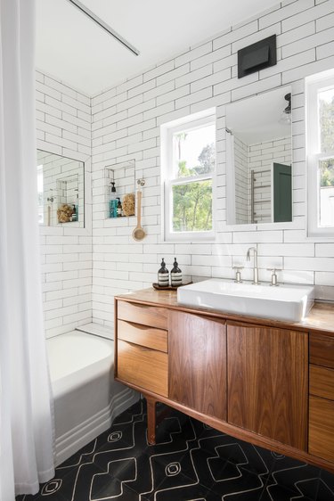 wood vanity with white vessel sink, black patterned floor tile, white subway tile walls, white shower curtain