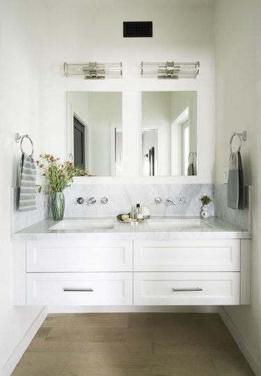 bathroom space with two mirrors, white cabinets, and hardwood floor
