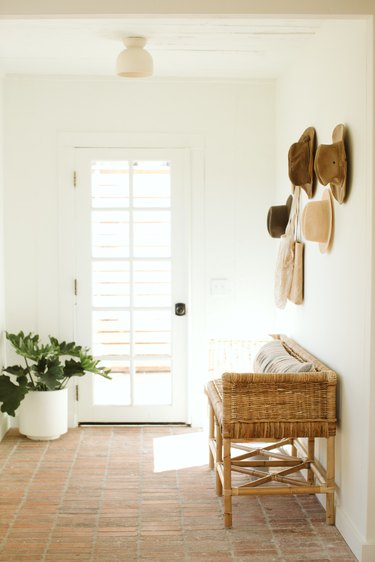 entryway idea with hats displayed on wall above accent bench with terra cotta flooring