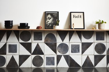 a wall of black and white geometric tile with black ceramics and pictures on the shelf