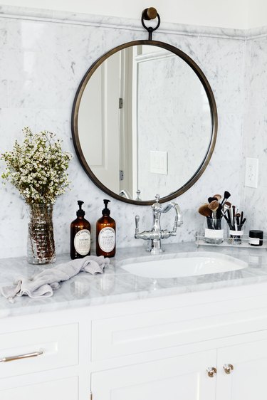 white bathroom with marble countertop and backsplash with round framed mirror