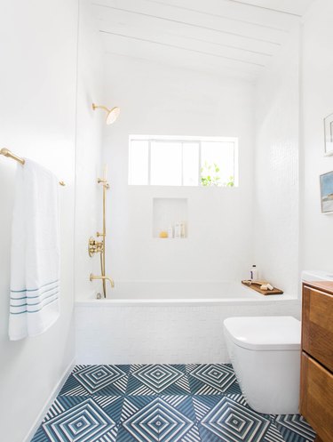 white bathroom with brass fixtures and blue patterned flooring