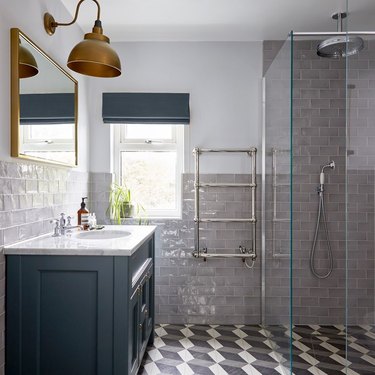 modern shower idea with patterned floor tile and blue cabinets and brass sconces