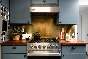 stainless steel gas range and vent hood, blue cabinets, smoke-effect backsplash