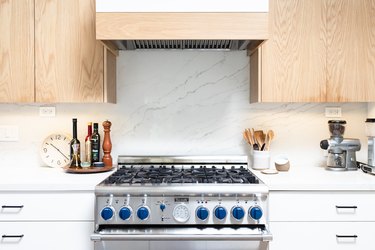 close up on stove with pale wood upper cabinets and white lowers