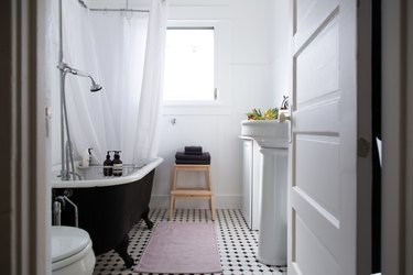 bathroom with pink rug, clawfoot tub, white walls