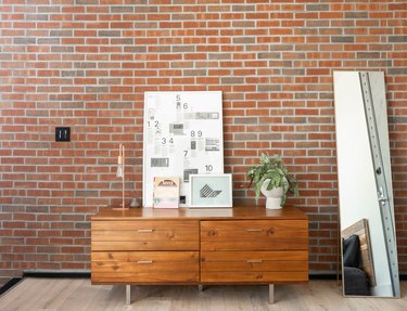 credenza in front of brick wall, mirror, artwork