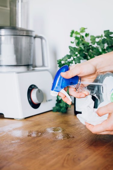 person spraying cleaner on a wood countertop