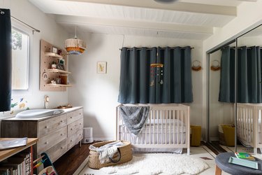 nursery space with wooden dresser, crib and dark blue curtain