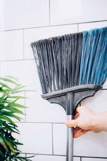 hand reaching for broom against white tiled wall