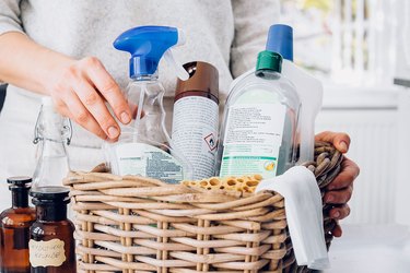 woman reaching for cleaner spray bottle in wicker basket of cleaning products