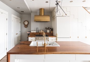 Kitchen with brass finish range hood, brass sink, wood counters.