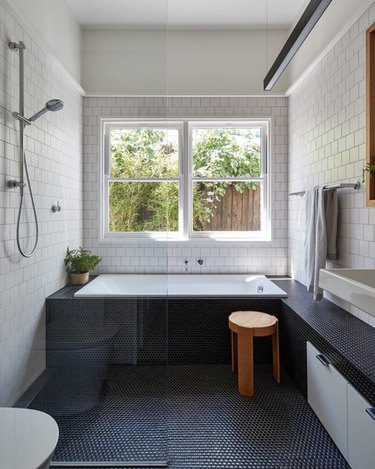 A shower and square tub in a master bathroom with white wall tile and grey floor tile.