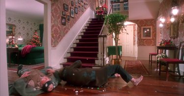 burglars fall on floor while little boy sits on stairs, still image from home alone set