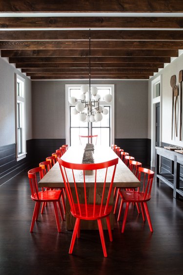 black dining room wainscoting with red chairs and wood beams by Chango & Co.