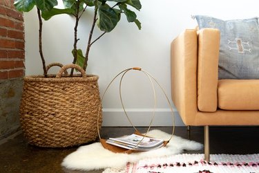 Leather and gold hoop magazine rack on sheepskin rug next to basket planter and plant.