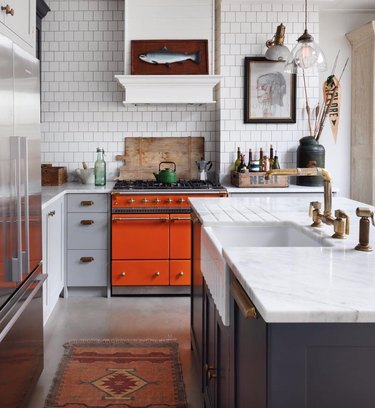 Red oven in kitchen with marble countertops and farmhouse sink.