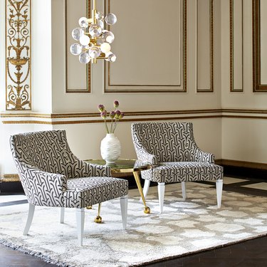 two patterned chairs with chandelier and white vase nearby