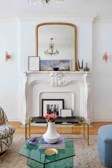 living room space with transparent green coffee table and gold mirror above closed fireplace