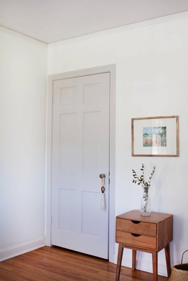 Door painted putty color, white walls, and wood side table with plant.