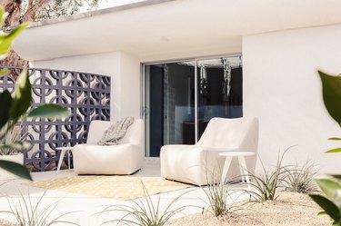 A retro gate with circles under an overhang of a modernist house Large chairs and small side tables. Plants line a rock garden.