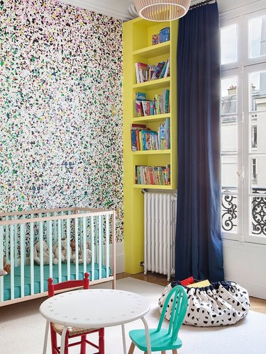 Splatter paint wallpaper in Paris nursery with yellow bookshelf.