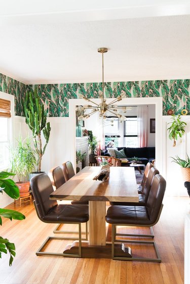 Tropical wallpaper in dining room with leather chairs and wood table.