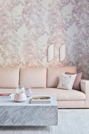 Wall sconce on floral wallpaper over pink couch.