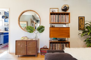 living room with bookshelves, round mirror, small credenza, view to blue cabinets in kitchen