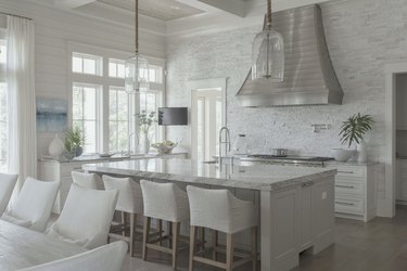 White kitchen with stainless hood, kitchen island, bar stools.