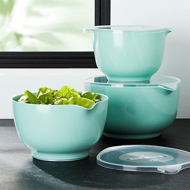 teal mixing bowls with clear lids on black counter