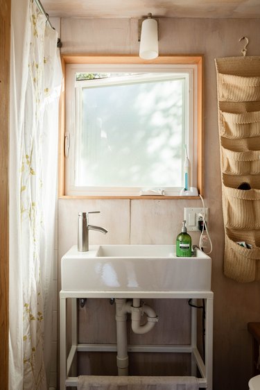 view of standing bathroom sink in front of an open window; electrical outlet with electric toothbrush plugged in