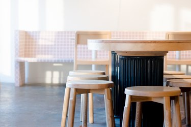 close up on table with wooden chairs, pink bench in background, concrete floors