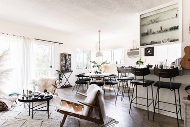 dining and living room with large windows and sheer curtains, black chairs, rug, concrete floors