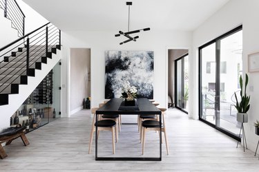 dining room with exposed stairs black table, large graphic artwork, hardwood floors