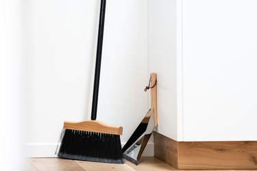 Broom and dustpan against white wall and wood floor