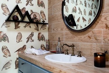 bathroom with owl wallpaper, round mirror and wood backsplash