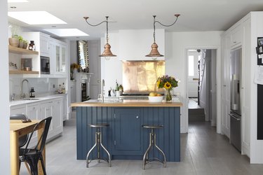 white kitchen with blue island and copper lighting above with copper backsplash