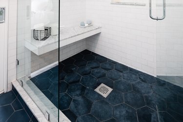 blue hexagon shower floor tile, silver square drain, built-in shower bench, glass shower door, white subway tile wall