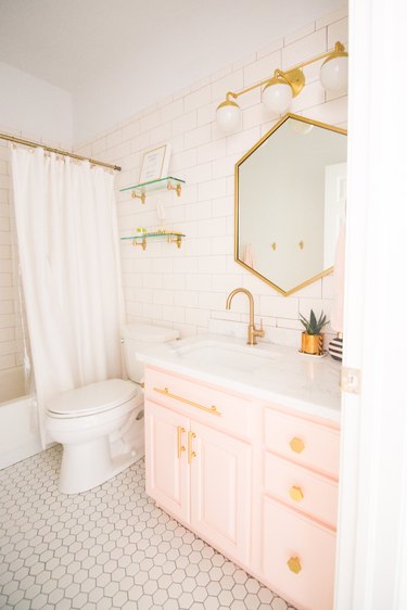Blush bathroom cabinets with geometric mirror and gold hardware