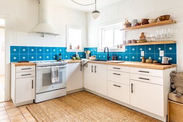 blue ceramic tiles above a wood countertop and white cabinetry with exposed shelving