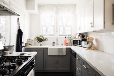 A small kitchen with sheer tied window treatments and gray lower cabinets