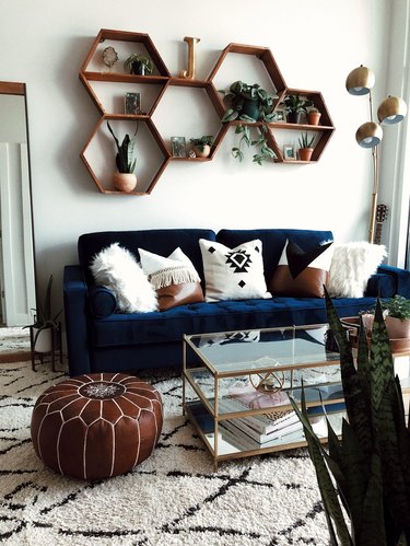 Boho apartment decor with navy blue couch, geometric shelving, and leather pouf in living room